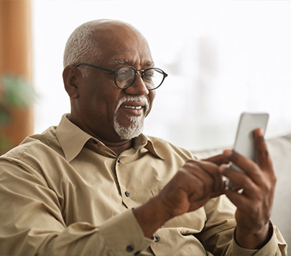 A senior man with eyeglasses, seated, using his smartphone.