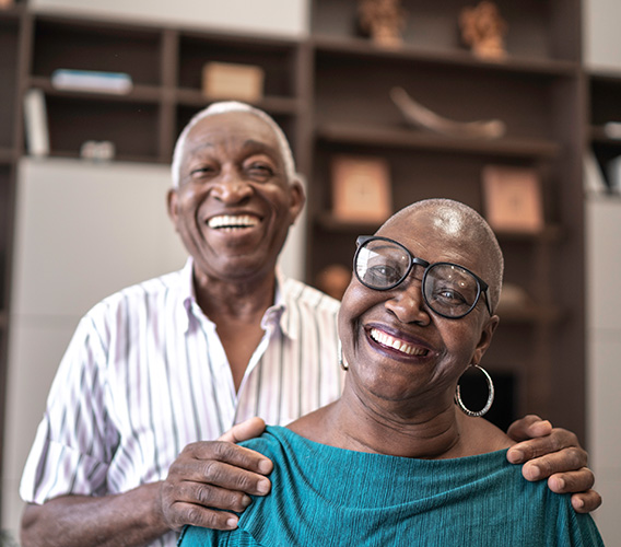 Two seniors, a man and a woman wearing glasses, smile at the camera.